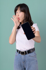 Naklejka premium Woman in a white t-shirt pointing at a smartphone with a happy expression on a green background, indicating joy and satisfaction.