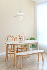 Modern dining area with wooden chairs, a bench, and a white table in a bright, cozy room.