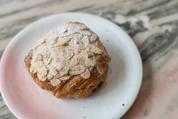 Almond croissant sprinkled with powdered sugar on cafe marble table