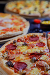 Hot tasty traditional various italian pizzas with salami, meat, cheese, onion, mushroom, tomatoes greens on a dark background