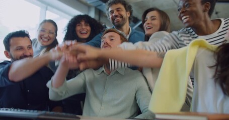 Camera focus of smart Caucasian male sitting in middle of his working team. Everyone smiling with joy after successful team building process. Raising their hands. Keyboard visible on desk. Office room