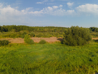 Landscape view from drone, yellow and green fields and haystacks, sky with white clouds. 