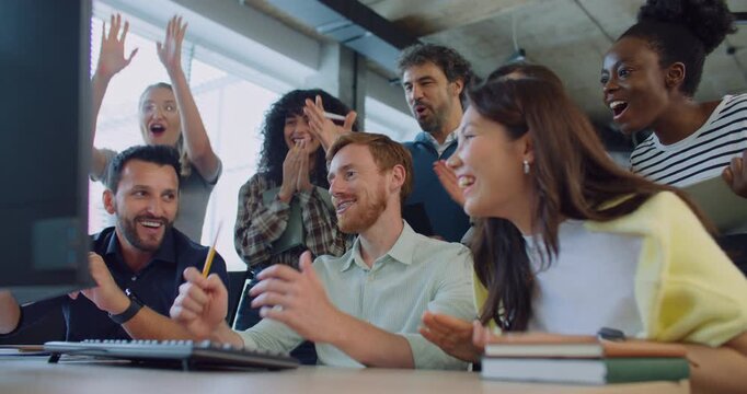 Multi-ethnic group of people at work. Looking patiently at screen. Waiting for important moment. After seeing positive result everyone exclaiming. Clapping their hands while smiling with joy.