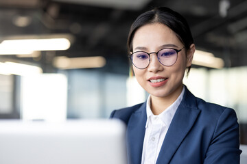 Professional Asian businesswoman in a bright, modern office setting, working confidently on her laptop. Capturing dedication, professionalism, and focus in a corporate environment.