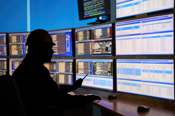 SCADA system in the central heating process.  Silhouette of an operator analyzing data on multiple...