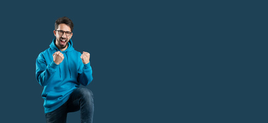 A young man is celebrating a personal achievement, raising his fists in triumph with a joyful...