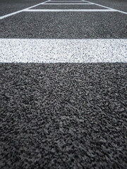Rubber Black Sports Track Surface with White Lines. Surface level view looking down the running track for the field jump event. Artificial textured surface with horizontal and vertical white lines.