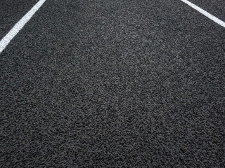 Fototapeta premium Rubber black running track surface with white lane lines. Surface level view of the textured artificial black surface.