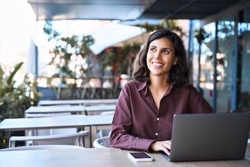Thoughtful young Arabic freelancer girl student using laptop pc for work sitting at desk outdoors....