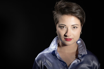 This image showcases a confident woman with short dark hair and an engaging smile, dressed in a shiny purple shirt, set against a professional, dark photographic backdrop.