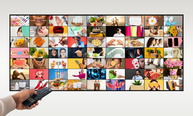 A persons hand holds a remote control, pointing towards a television screen. The screen displays a grid of many diverse images, including people, food, nature, and objects.