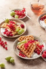 Homemade waffles with summer berries and yogurt served for sweet breakfast with tea on beige background. Heart shaped waffles