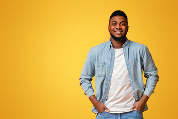 Fototapeta premium Portrait of confident african american man standing with hands in pockets on yellow background with free space