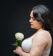 Beautiful woman in lingerie with a rose in her hands posing in a dark studio. She is wearing a white bra and black tights.