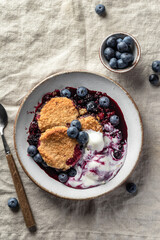 Homemade blueberry cobbler pie served with scoop of ice cream in ceramic plate on linen tablecloth table top view, flatly, sweet breakfast