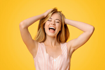 Fototapeta premium Expression Of Joy. Young girl emotionally shouting with closed eyes, standing over yellow background in studio, copy space