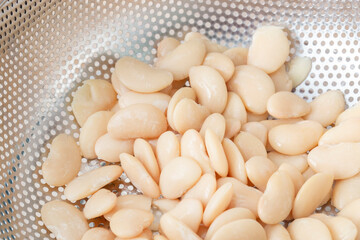 Straining butter beans in a metal colander strainer. Vegan healthy diet food ingredients.