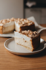 A slice of delicious homemade baked cheesecake with creamy meringue texture dessert decorated with walnuts on top filled with tasty flavors and caramel drops on craft bakery paper standing on a wooden
