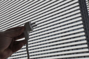 human hand holding Electric plug on highrise building background. fingers with plug on building...