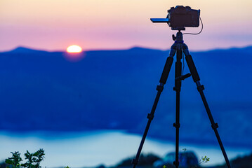 Camera on tripod taking picture of sunset over sea