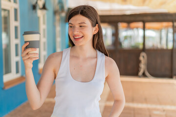 Young pretty Ukrainian woman holding a take away coffee at outdoors with happy expression