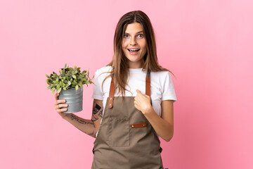 Gardener woman holding a plant isolated on pink background with surprise facial expression