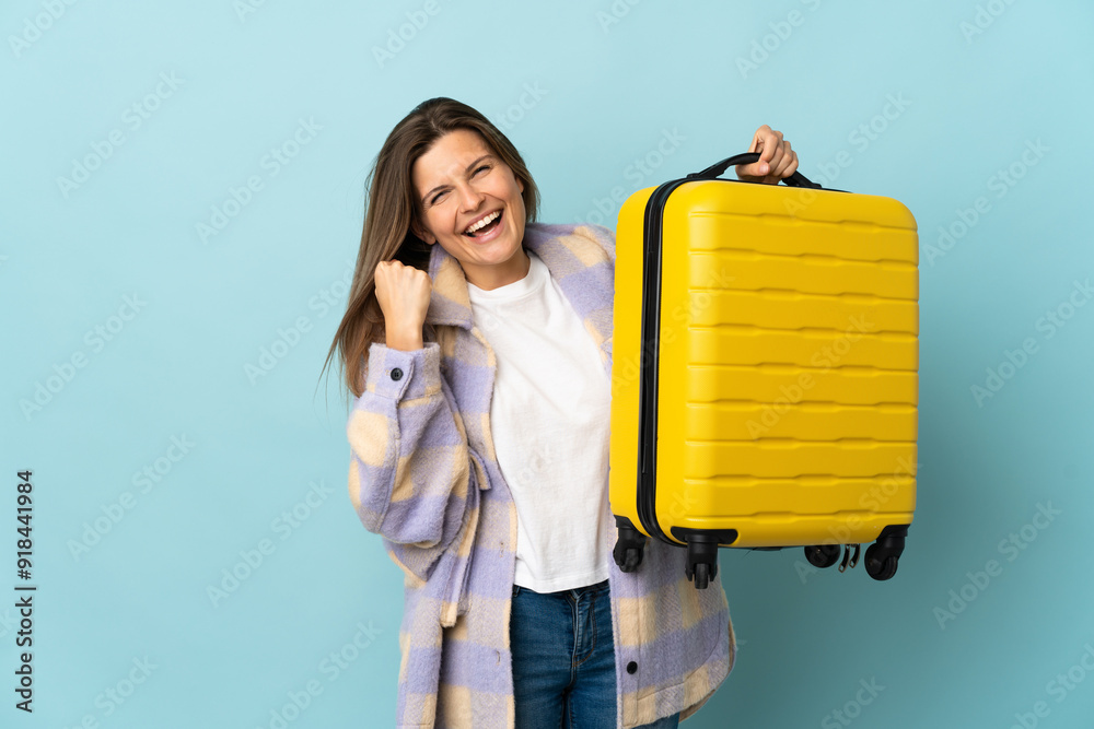 Wall mural young slovak woman isolated on blue background in vacation with travel suitcase