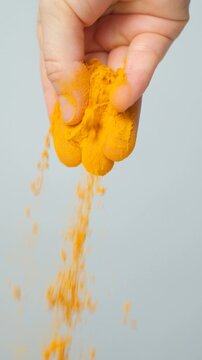 Hand pouring turmeric powder, vertical slow motion.