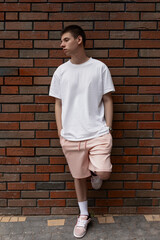 young guy fashionably dressed in summer clothes on background dark brick wall outdoors