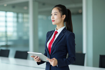 Obraz premium photo of woman in navy suit outfit and red tie holding tablet in the office, generative AI