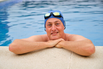 Swimmer is taking a break from his training, resting his arms on the poolside