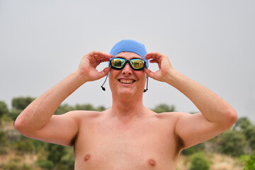 Male swimmer with blue swim cap smiling while adjusting goggles outdoors before a swimming competition