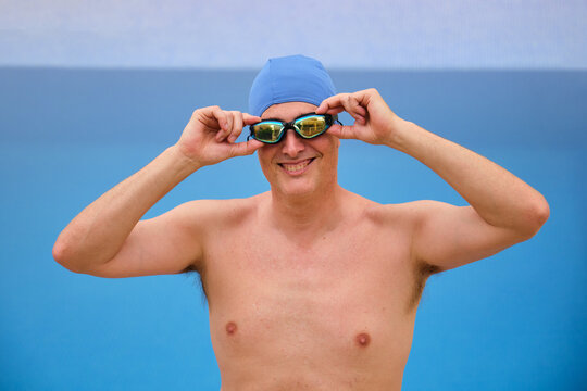 Male swimmer is adjusting his swimming goggles and smiling before diving into the pool