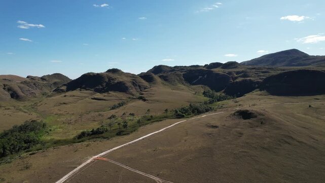 aerial video of cerrado fields, with dirt road, hills, Chapada dos Veadeiros, Goi&aacute;s, Brazil
