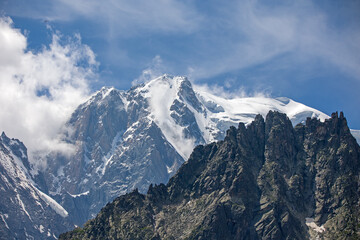view of the mont blanc massif from the italian side with snow-covered peak and blue cloudy sky in the foreground a dark mountain