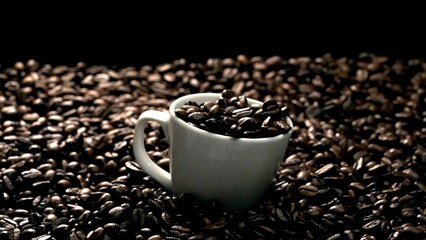 Close up of coffee bean falling in to coffee cup surrounded by pile of beans. Dropping aromatic blending bean in to white cup. Top view of coffee drop in to glass with black background. Comestible.
