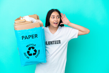 Teenager girl with braids holding a bag to recycle listening to something by putting hand on the ear