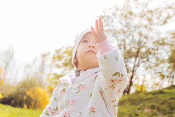 Cheerful toddler girl in white floral jumpsuit sitting in pine forest park. Family lifestyle,...