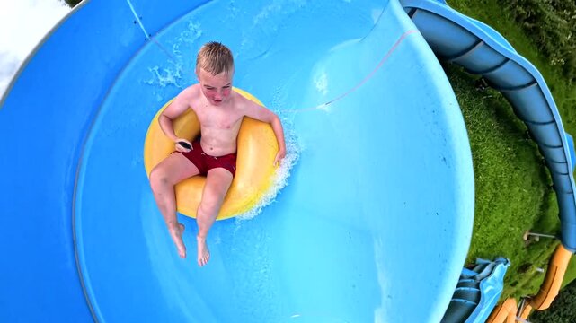 Joyful boy slides down the blue water slide