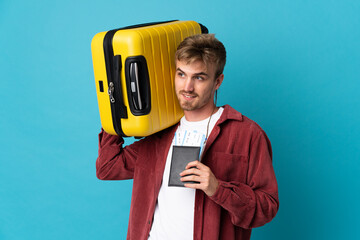 Young handsome blonde man isolated on blue background in vacation with suitcase and passport