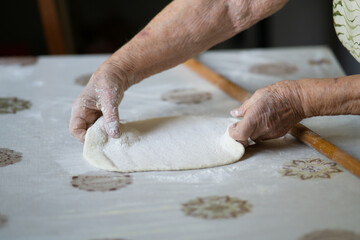close up of grandmother's old wrinkled hands rolling dough with a rolling pin. Elderly woman rolling out dough with a rolling pin