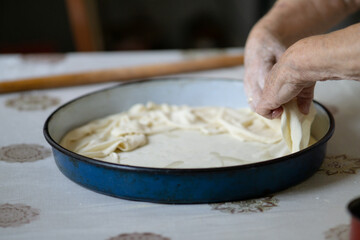 Old grandmother putting rolled dough in a pan. Elderly woman making traditional balkan pie