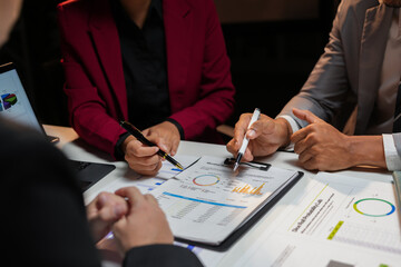 Business team working late, analyzing financial data and pointing at charts with pens during a meeting in the office