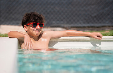Smiling teenager boy sitting in a pool relaxed