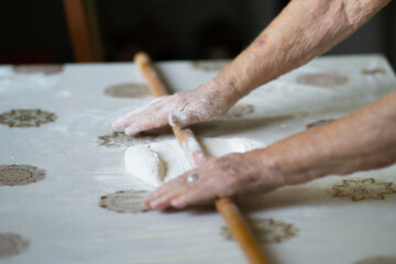 close up of grandmother's old wrinkled hands rolling dough with a rolling pin. Elderly woman rolling out dough with a rolling pin
