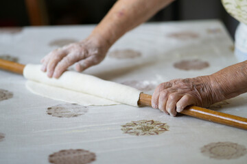 close up of grandmother's old wrinkled hands rolling dough with a rolling pin. Elderly woman rolling out dough with a rolling pin