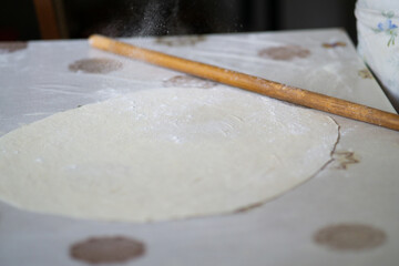 Rolled out dough and rolling pin on a table. Pouring flour on the dough