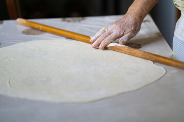 close up of grandmother's old wrinkled hands rolling dough with a rolling pin. Elderly woman rolling out dough with a rolling pin