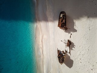 Aerial view of a shipwreck on a sandy beach with clear blue water.