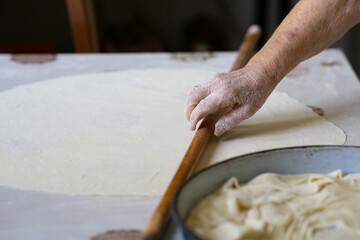close up of grandmother's old wrinkled hands rolling dough with a rolling pin. Elderly woman rolling out dough with a rolling pin